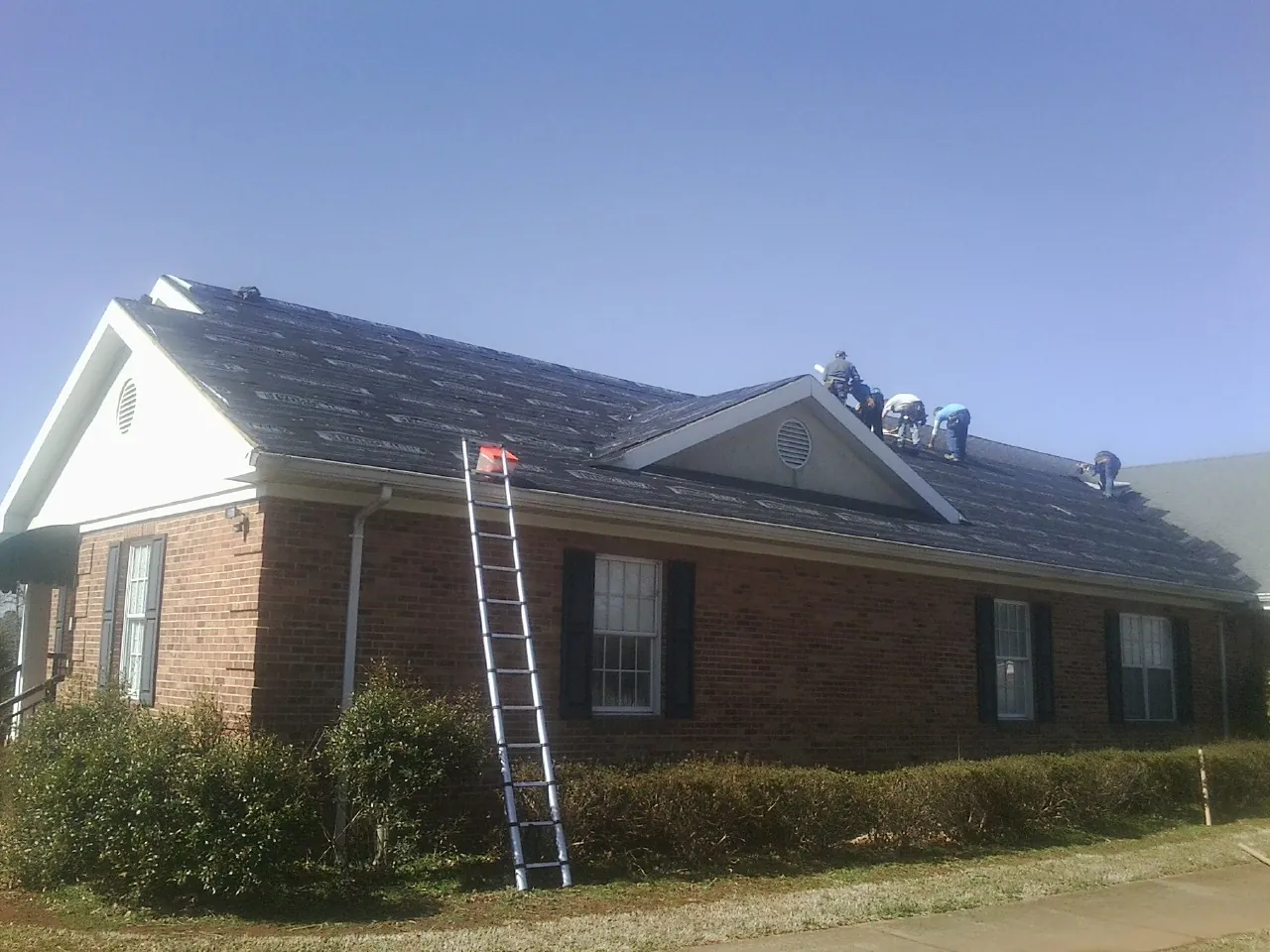 Crew tearing shingles off a brick ranch roof with a ladder set — Emergency Roof Repair work by our crew in Cheshire