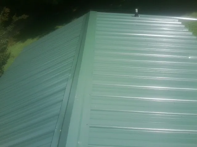New green metal panels meeting at the ridge of a roof — Flat Roof Repair work by our crew in Cheshire