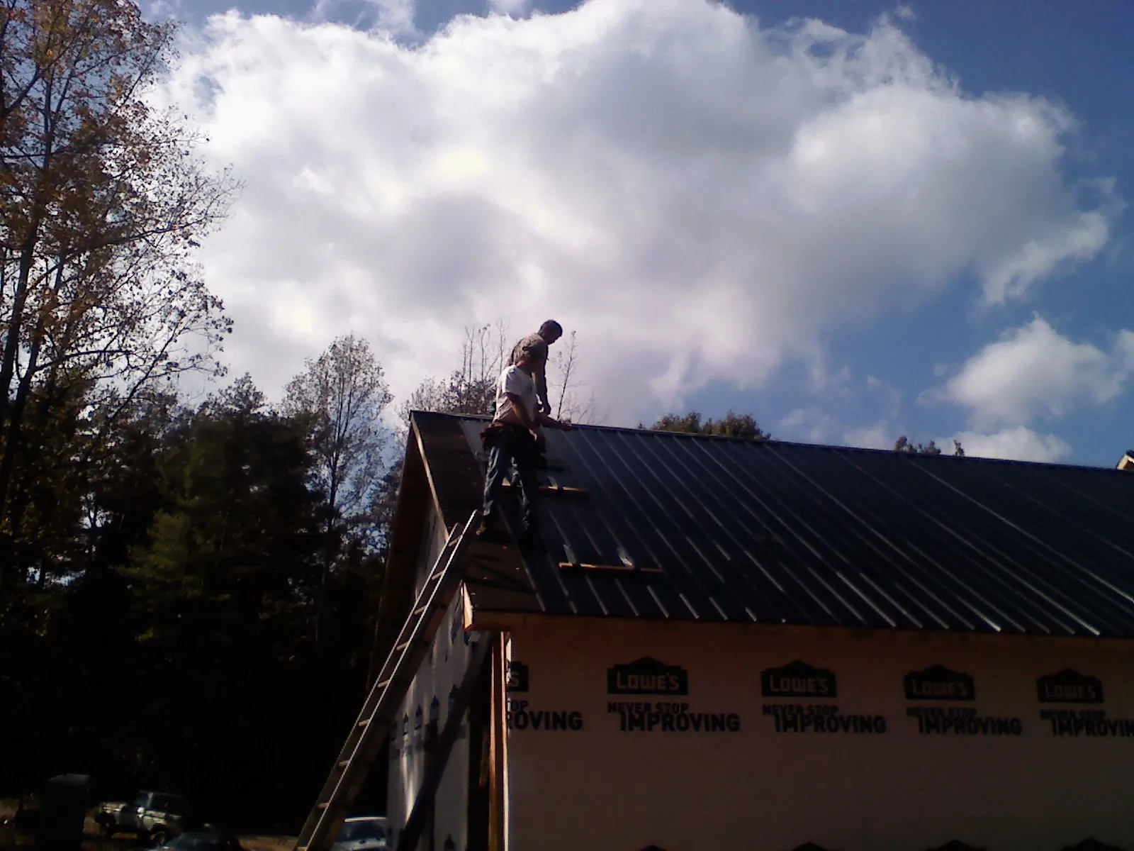 Roofer fastening dark metal panels high against a cloudy sky, from a Roof Inspection job in Cheshire