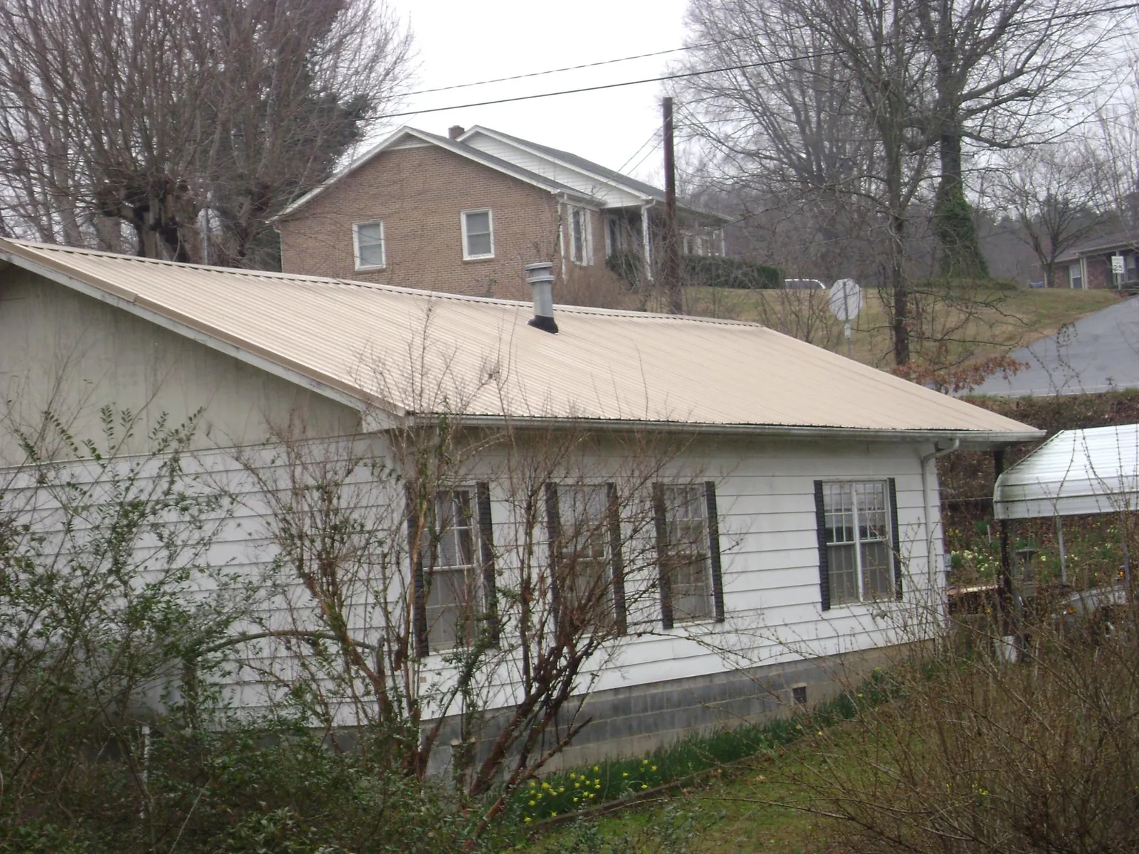 Tan metal roof on a white sided house set into a hillside — Commercial Roofing by Roofing Brothers in Cheshire